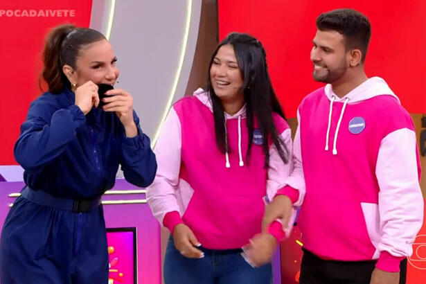 Ivete Sangalo de macaquito jeans azul, mordendo a aliança ao lado do casal Tamires e Anderson durante gravação do Pipoca da Ivete, da TV Globo