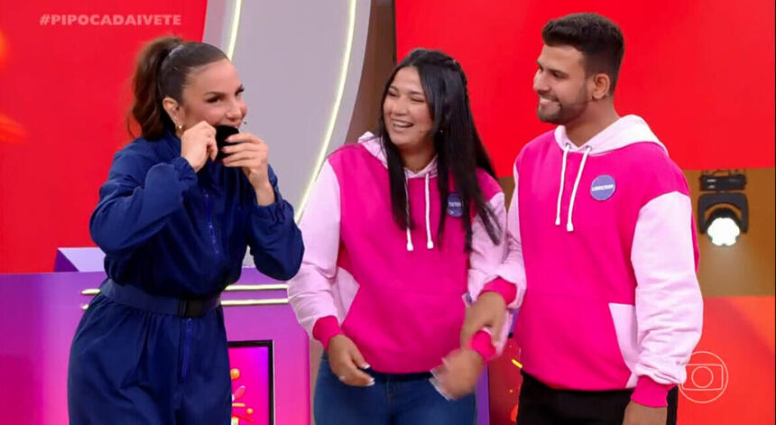 Ivete Sangalo de macaquito jeans azul, mordendo a aliança ao lado do casal Tamires e Anderson durante gravação do Pipoca da Ivete, da TV Globo