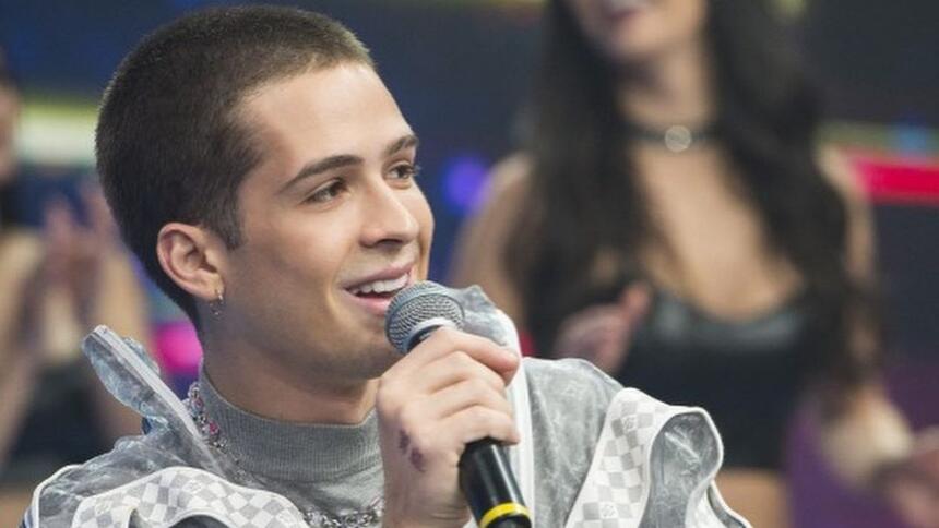 João Gomes sorrindo segurando o microfone com a mão direita durante gravação do Faustão na Band