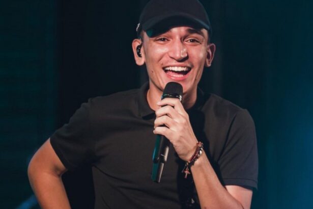 João Gomes sorrindo, de camisa e boné preto, segurando microfone durante show