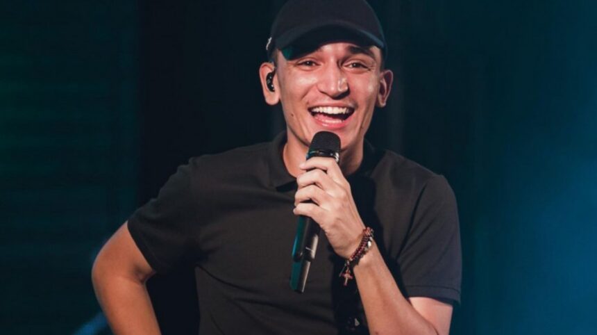 João Gomes sorrindo, de camisa e boné preto, segurando microfone durante show