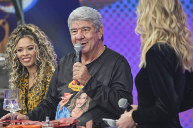 Juliana Diniz com body animal print, cabelo preso, sorrindo, ao lado de joel santana; joel Santana de camisa preta, segurando um microfone na mão esquerda, sentado durante gravação do Faustão na Band