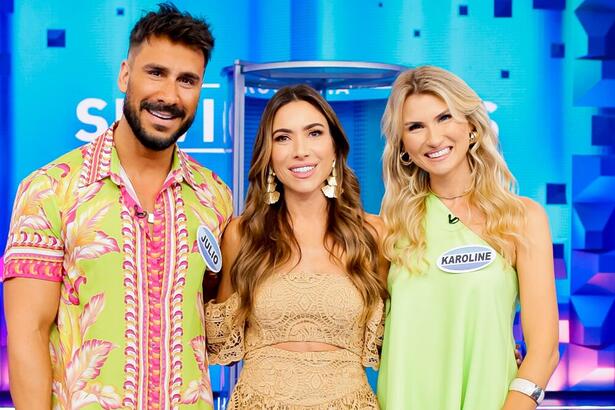 Júlio Rocha de camisa e bermuda estampada das cores vermelho, rosa e amarelo, sorrindo; Karoline Kleine de vestido verde claro, sorrindo; Patricia Abravanel de vestido bege, com brincos dourados, cabelo solto, sorrindo, durante gravação do Programa Silvio Santos, do SBT