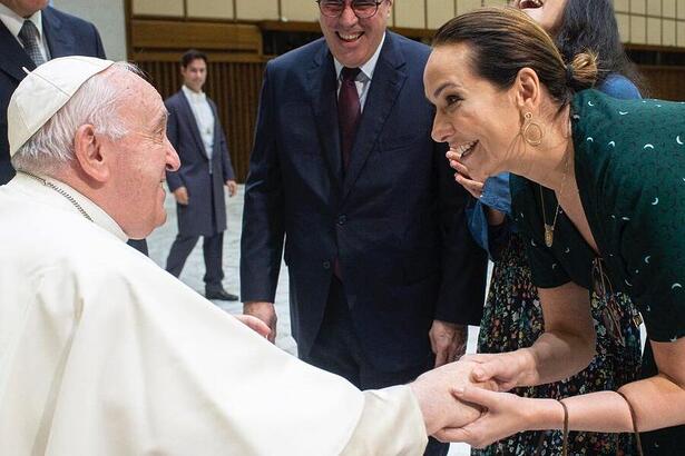 Maria Beltrão de vestido veste, abaixada segurando a mão do Papa Francisco durante encontro com o Papa Francisco no Vaticano