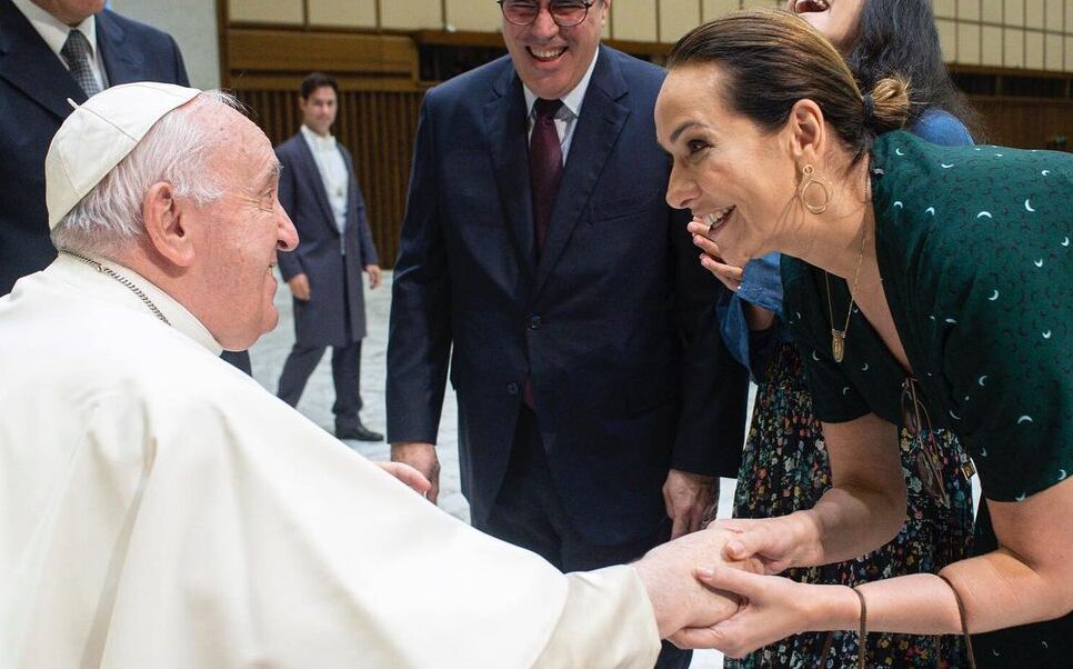 Maria Beltrão de vestido veste, abaixada segurando a mão do Papa Francisco durante encontro com o Papa Francisco no Vaticano