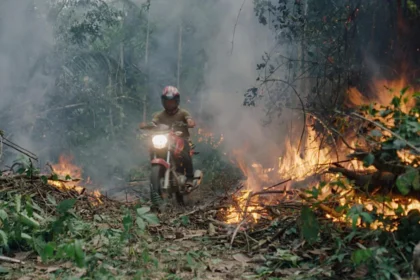 Uma moto passando em volta de terras pegando fogo, em trecho do filme O Território