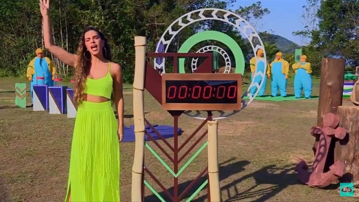 Mariana Rios de vestido verde ao lado de um cronometro no local de provas.