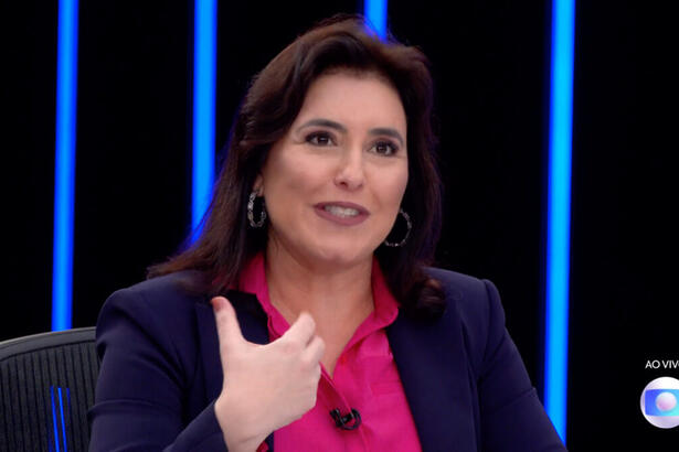 Simone Tebet de blazer azul e camisa rosa, sentada durante entrevista no JN