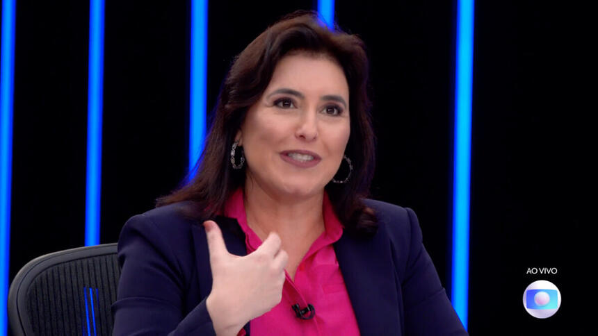 Simone Tebet de blazer azul e camisa rosa, sentada durante entrevista no JN