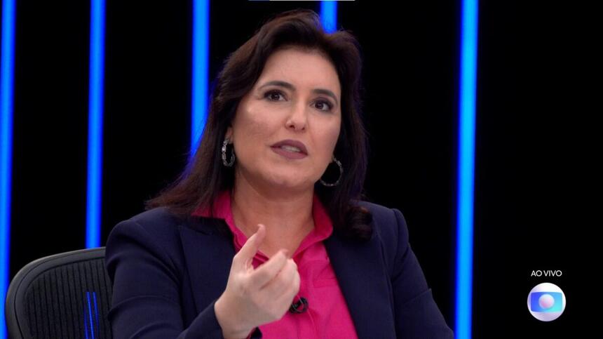 Simone Tebet de blazer azul e camisa rosa, sentada durante entrevista no JN