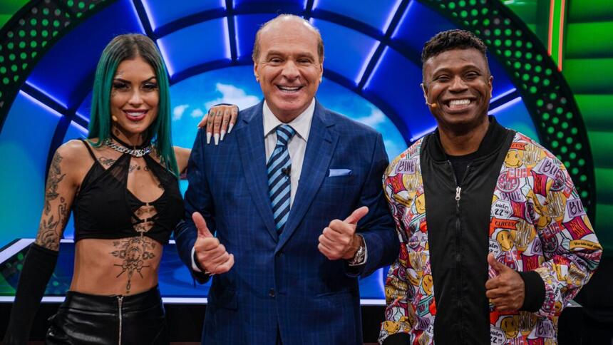 Tati Zaqui sorrindo, com look em decote preto, com a mão no ombro de Marcelo; Edilson Capetinha com blazer em estampa colorida e camisa preta, colar de prata, sorrindo; Marcelo de Carvalho no centro de blazer e gravata azul e camisa social branca fazendo um legal com as duas mãos durante gravação de O Céu é o Limite, da RedeTV!