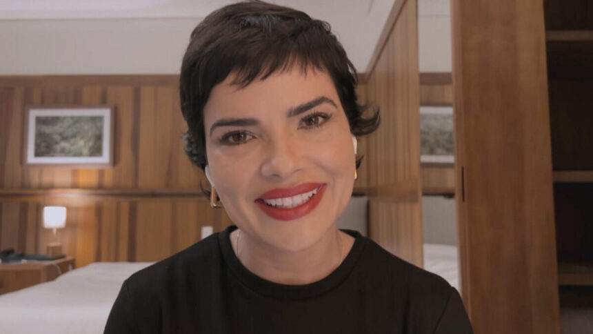 Vanessa Giácomo de cabelo curto para novo personagem, sorrindo, de batom vermelho e camisa preta durante entrevista para Pedro Bial