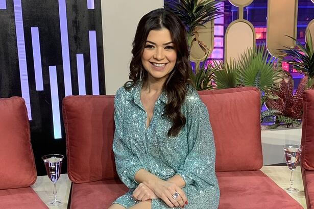 Amanda Françozo de vestido azul claro, sentada, com as mãos juntas, sorrindo durante gravação do De Papo com Amanda Françozo, da TV Aparecida