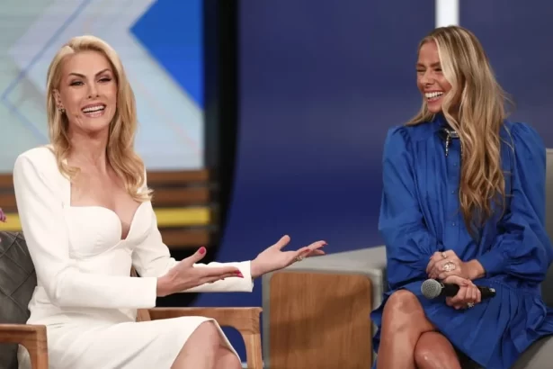 Ana Hickmann de vestido branco, com plaquinhas no banco, sorrindo, de cabelo solto, ao lado de Adriane Galisteu; Adriane Galisteu de vestido azul, cabelo solto, sorrindo durante entrevista em coletiva de A Fazenda no Hoje em Dia, da Record TV