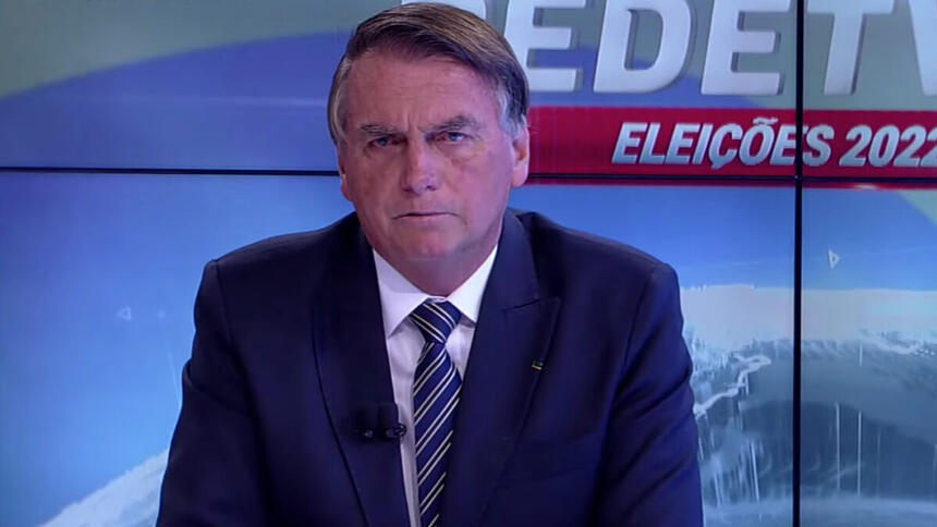 Bolsonaro de palitó, preto, gravata listrada preta a branca, camisa social branca, sentado durante entrevista na RedeTV!