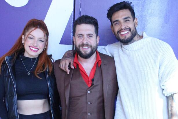 Brenda Paixão de top e calça preta, jaqueta e capuz preto, batom vermelho, cabelo preso, sorrindo; Mauricio Meirelles de camisa social vermelha, colete e blazer marrom, sorrindo; matheus Sampaio de camisa branca, sorrindo, durante gravação do Foi Mau, da RedeTV!