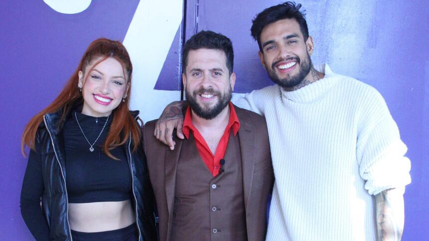 Brenda Paixão de top e calça preta, jaqueta e capuz preto, batom vermelho, cabelo preso, sorrindo; Mauricio Meirelles de camisa social vermelha, colete e blazer marrom, sorrindo; matheus Sampaio de camisa branca, sorrindo, durante gravação do Foi Mau, da RedeTV!