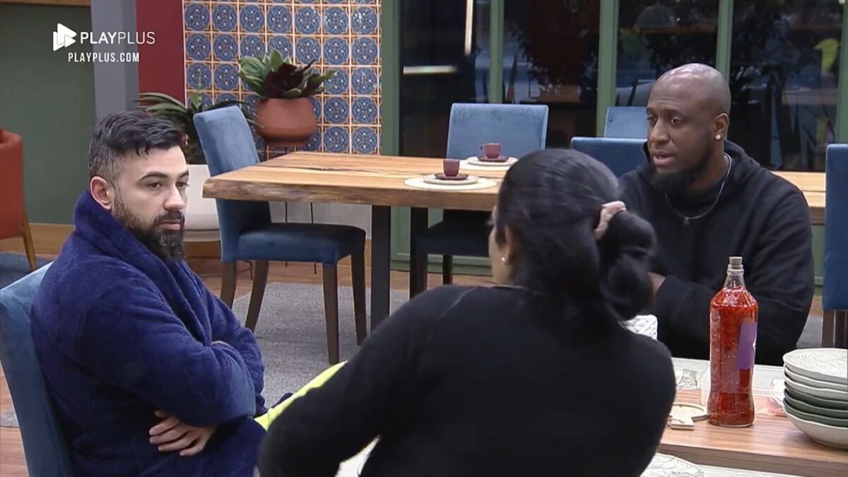 Bruno sentado na mesa de A Fazenda ao lado de André Marinho e Rosiane Pinheiro.