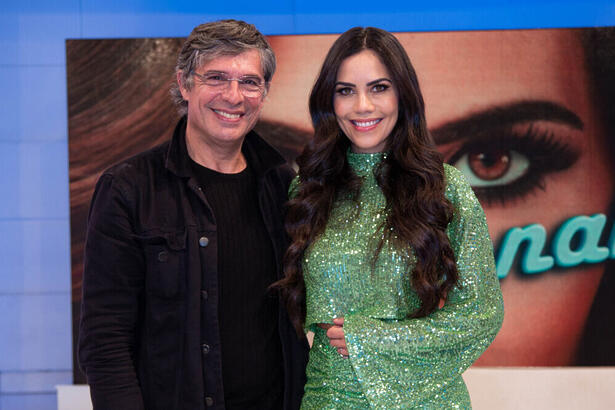 Chef Oliver Anquier de camisa preta, sorrindo, usando óculos de grau, abraçado com Daniela Albuquerquer, de vestido verde, cabelo solto, sorrindo, durante gravação do Sensacional, da RedeTV!