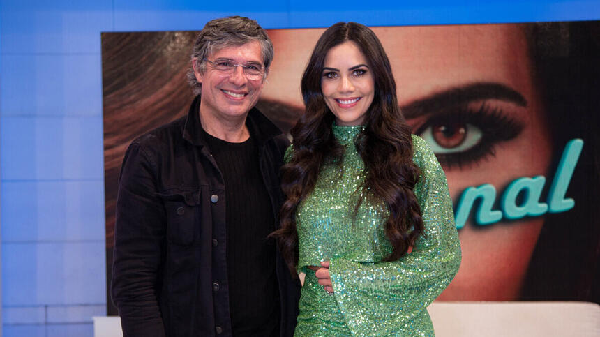 Chef Oliver Anquier de camisa preta, sorrindo, usando óculos de grau, abraçado com Daniela Albuquerquer, de vestido verde, cabelo solto, sorrindo, durante gravação do Sensacional, da RedeTV!