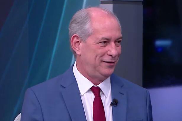 Ciro Gomes de palitó azul, gravata vermelha e camisa social branca, sentado durante entrevista na CNN Brasil