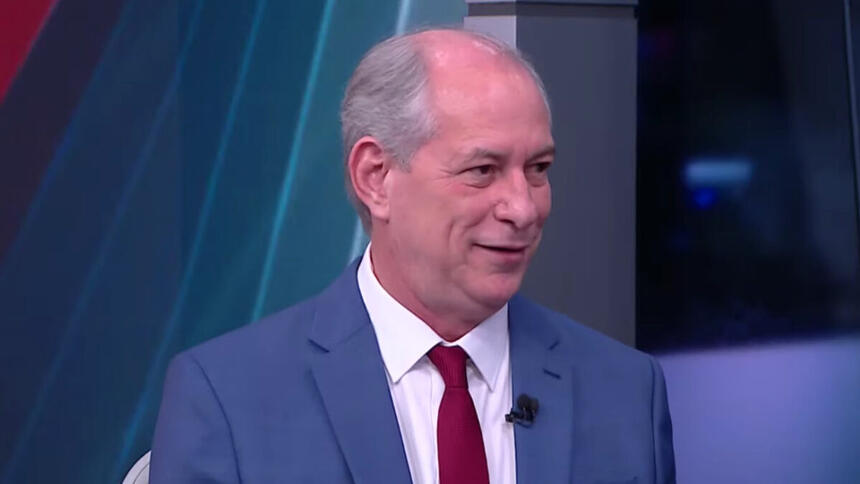 Ciro Gomes de palitó azul, gravata vermelha e camisa social branca, sentado durante entrevista na CNN Brasil