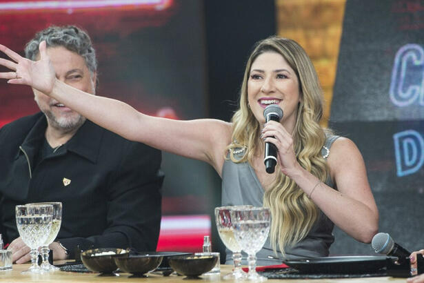 Dani Calabresa de camisa cinza, com os braços abertos, sorrindo, segurando o microfone