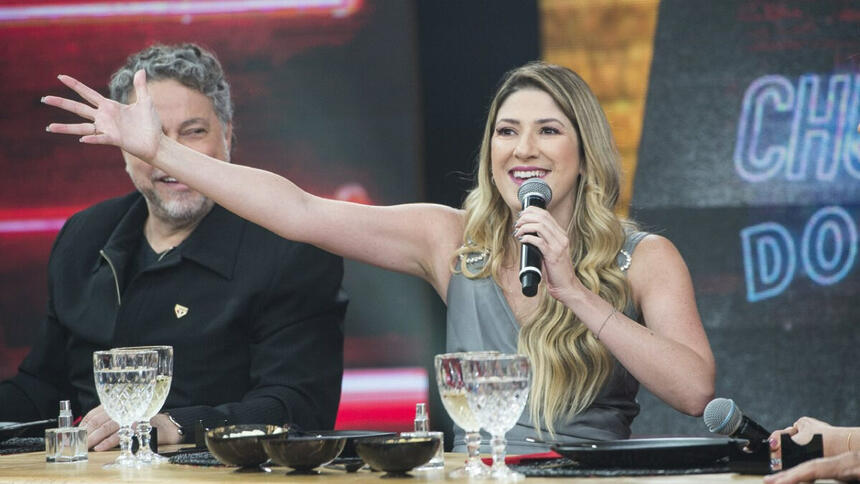 Dani Calabresa de camisa cinza, com os braços abertos, sorrindo, segurando o microfone