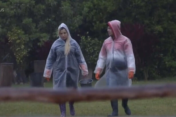 Deolane Bezerra e Lucas Santos, com capas de chuva, durante o trato dos animais em A Fazenda 14