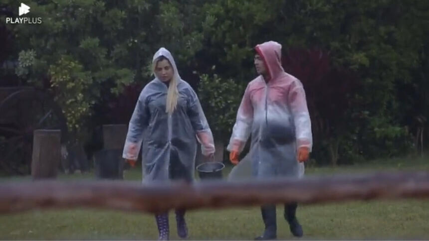 Deolane Bezerra e Lucas Santos, com capas de chuva, durante o trato dos animais em A Fazenda 14