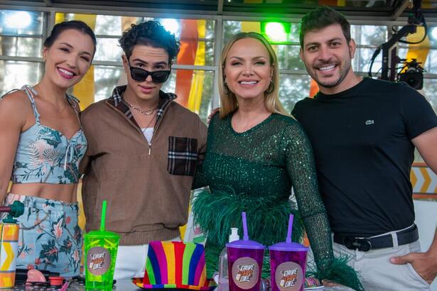 Eliana sorrindo, de vestido verde, atrás de mesa com adereços; Igor Jansen de camisa marrom e calça branca, usando oculos de sol preto; Bia Napolitano de vestido estampado, sorrindo; Caio Afiune sorrindo, de camisa preta, usando barba