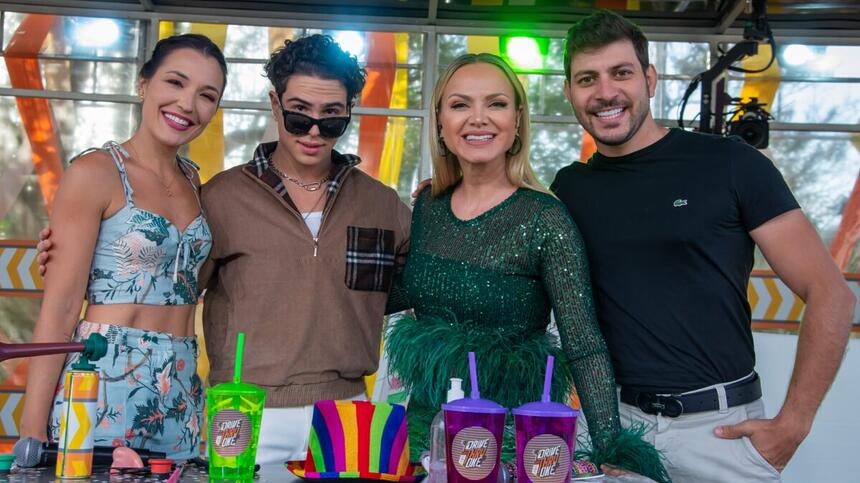 Eliana sorrindo, de vestido verde, atrás de mesa com adereços; Igor Jansen de camisa marrom e calça branca, usando oculos de sol preto; Bia Napolitano de vestido estampado, sorrindo; Caio Afiune sorrindo, de camisa preta, usando barba