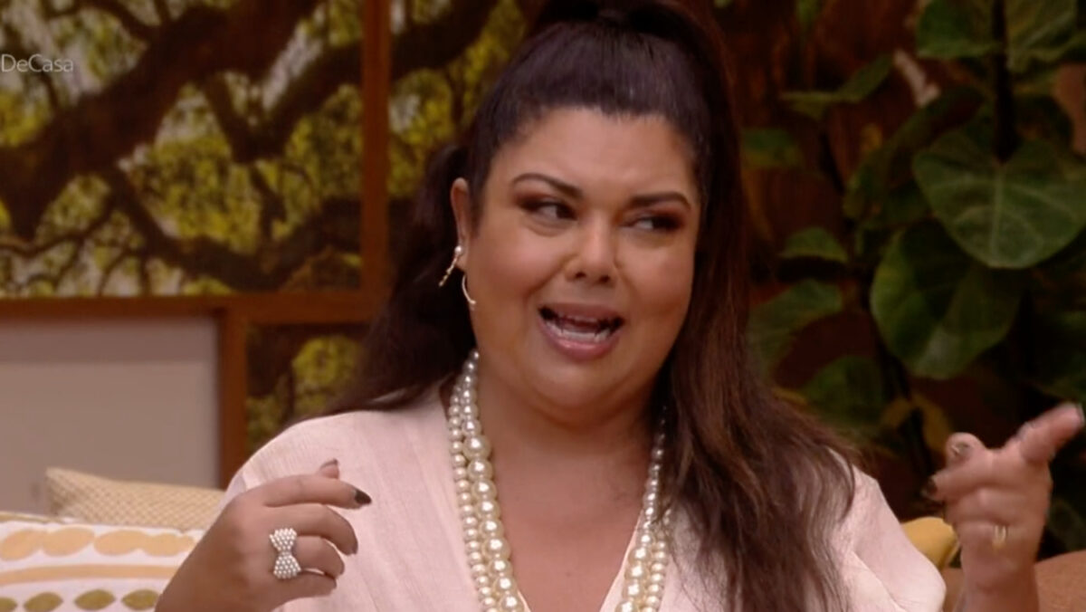 Fabiana Karla de look rosa claro, cabelo preso (rabo de cavalo) apontando com a mão esquerda