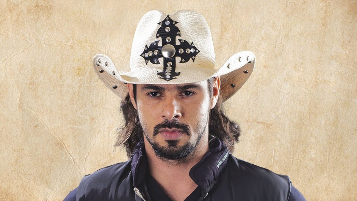João Carreiro de chapéu de cowboy, camisa social azul, de cabelo solto, bigode e calvanhaque para ensaio fotográfico