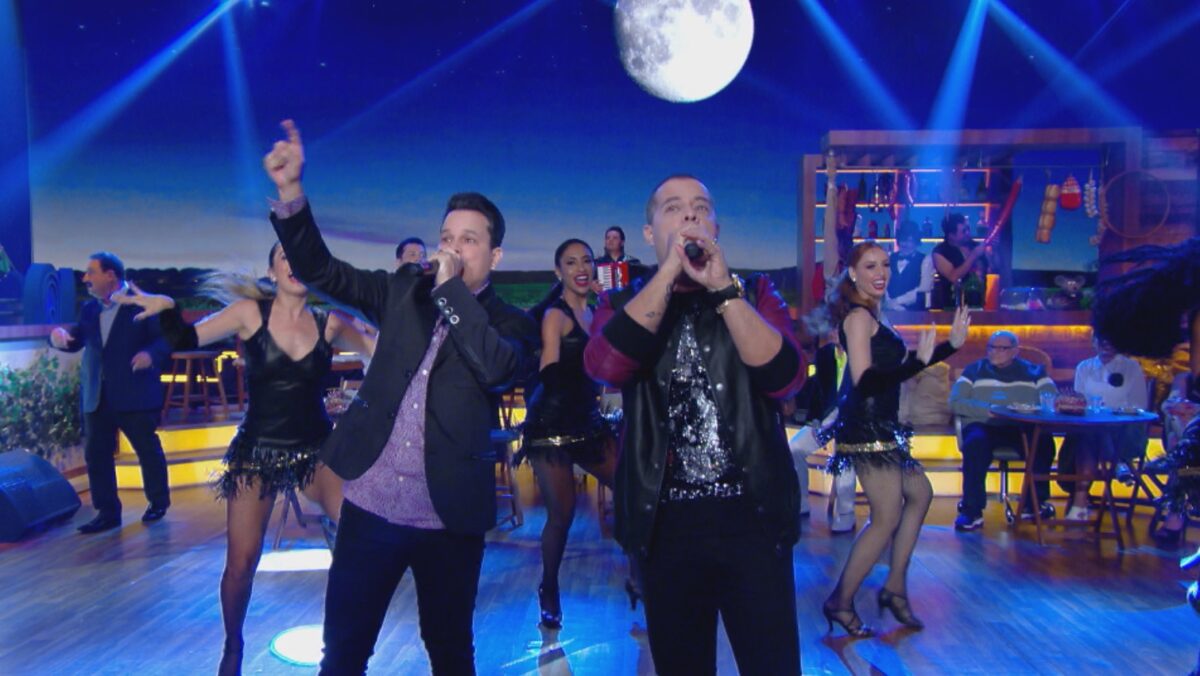João Neto e Frederico de jaqueta e calça jeans preta com microfone na mão durante gravação de performance no Boteco do Ratinho, do SBT