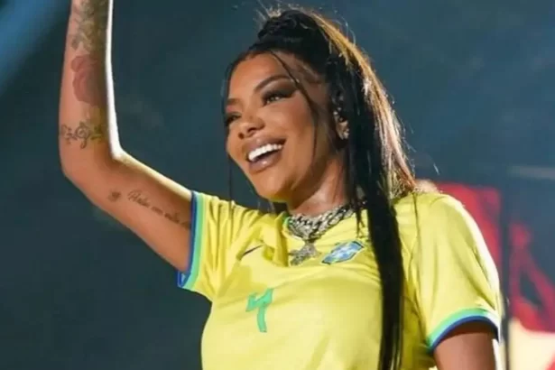 Ludmilla com o braço direito levantado, sorrindo, lace preta presa, usando camisa do brasil durante performance no Rock in Rio