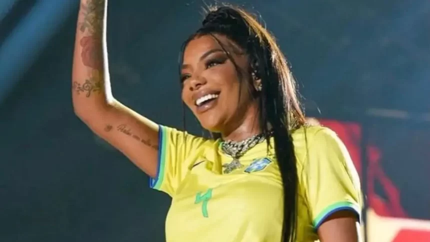 Ludmilla com o braço direito levantado, sorrindo, lace preta presa, usando camisa do brasil durante performance no Rock in Rio