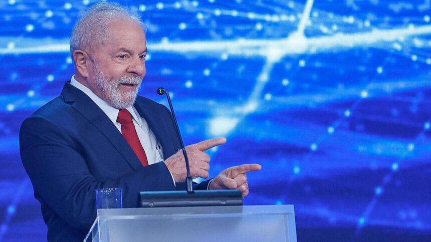 Lula de blazer azul, gravata vermelha e camisa social branca, apontando durante debate na Band