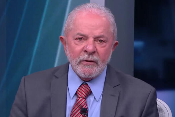 Lula de palitó cinza, gravata magenta e camisa social azul, com as mãos juntas, durante gravação da sabatina da CNN Brasil