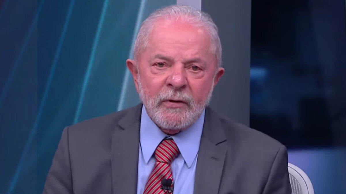 Lula de palitó cinza, gravata magenta e camisa social azul, com as mãos juntas, durante gravação da sabatina da CNN Brasil