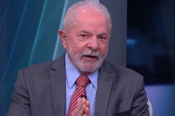 Lula de palitó cinza, gravata magenta e camisa social azul, com as mãos juntas, durante gravação da sabatina da CNN Brasil