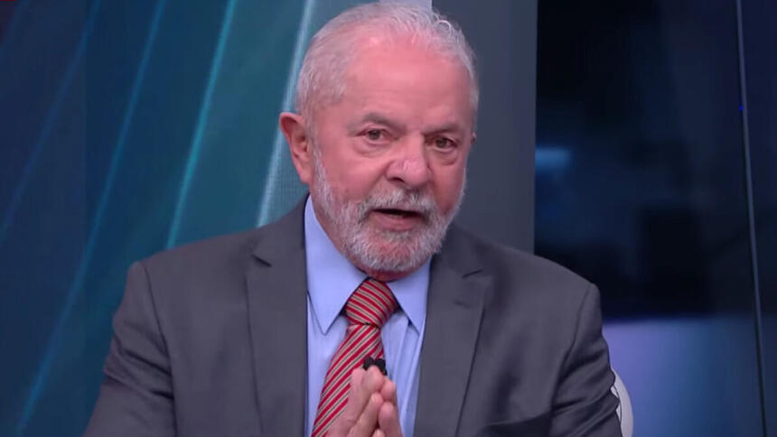 Lula de palitó cinza, gravata magenta e camisa social azul, com as mãos juntas, durante gravação da sabatina da CNN Brasil