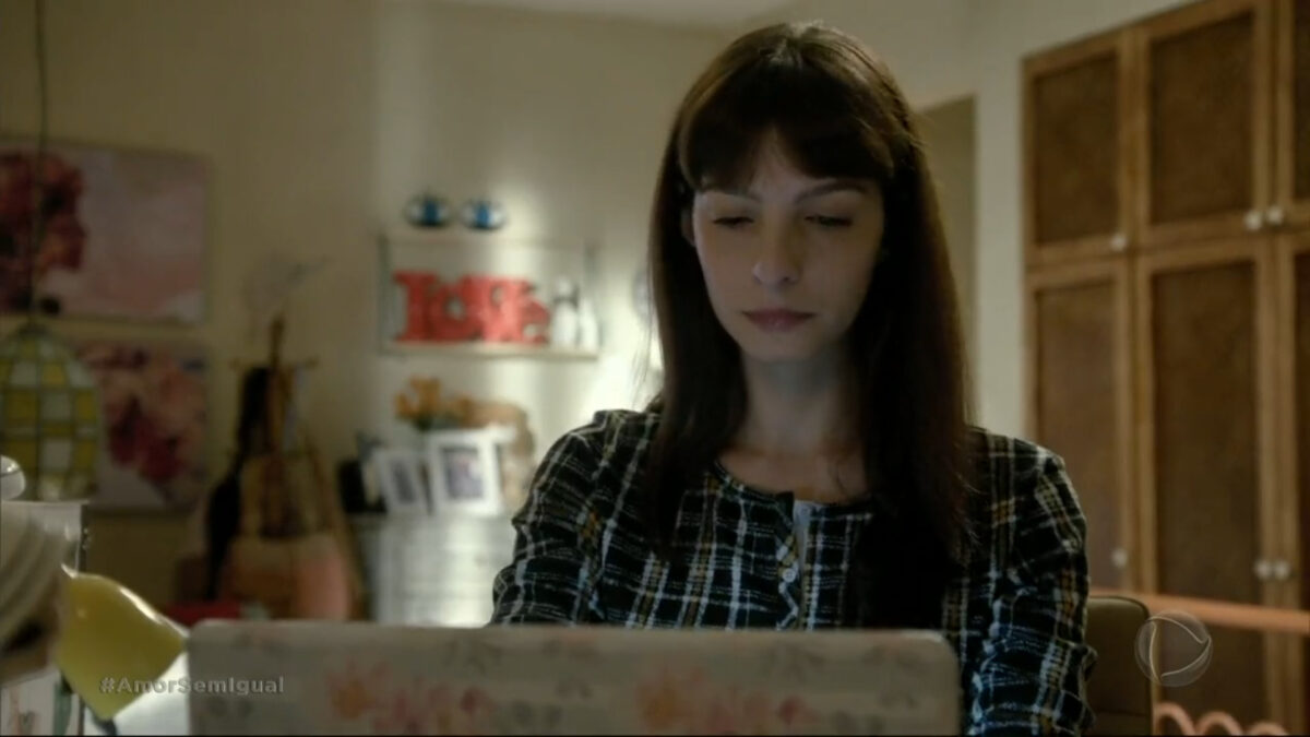 Atriz Michelle Batista, como Maria Antonia, em trecho da novela Amor sem Igual. A personagem está em frente a um notebook