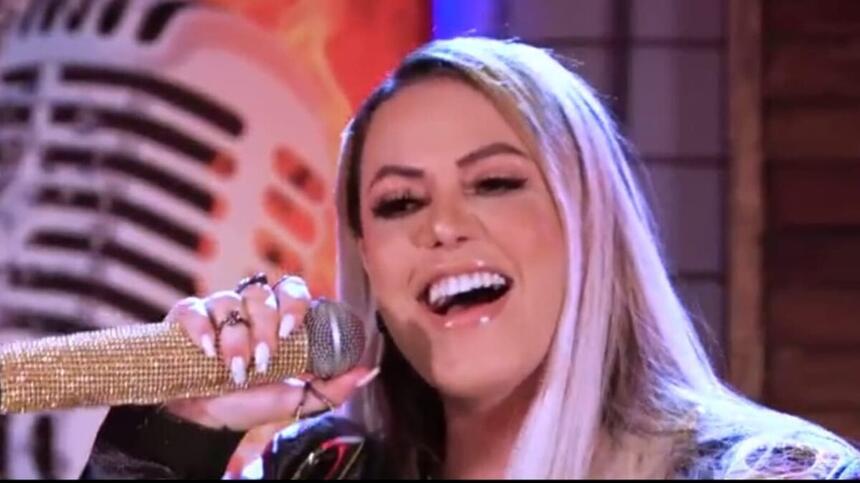 Michelle Melo de cabelo solto, boca aberta, com microfone dourado próximo; durante gravação do EP Risco de Embriaguez