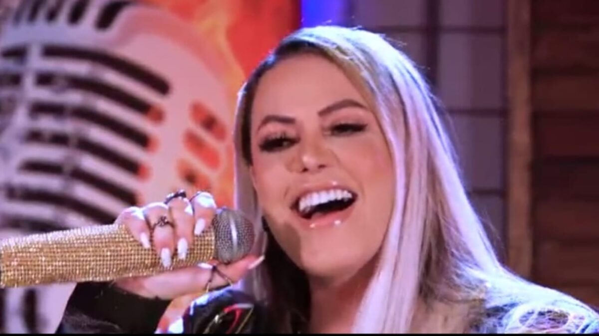 Michelle Melo de cabelo solto, boca aberta, com microfone dourado próximo; durante gravação do EP Risco de Embriaguez