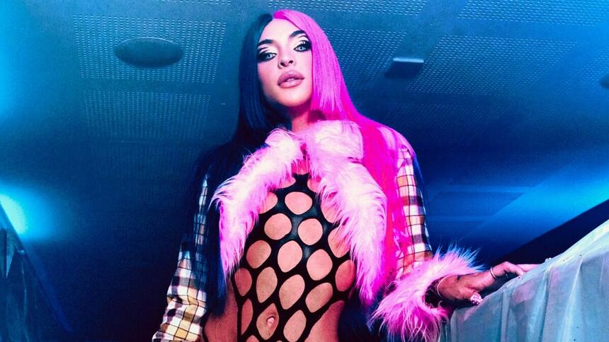 Pabllo vittar de lace rosa e azul, com pluma rosa, colante preto durante ensaio fotográfico de divulgação de "Descontrolada"