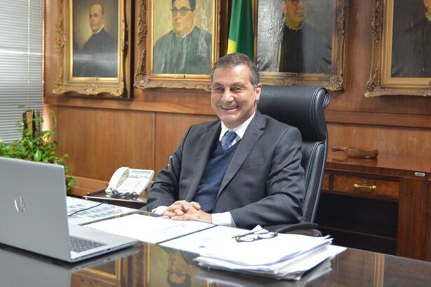 Paulo Galizia sentado em uma mesa, em frente a um notebook