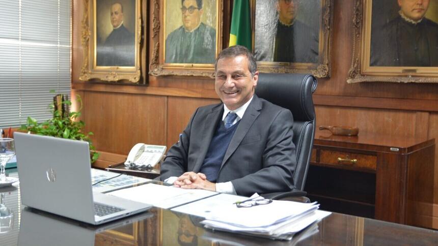 Paulo Galizia sentado em uma mesa, em frente a um notebook