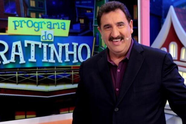 Ratinho de blazer preto e camisa social marrom, sorrindo, de perfil, microfone no rosto durante gravação de seu programa no SBT