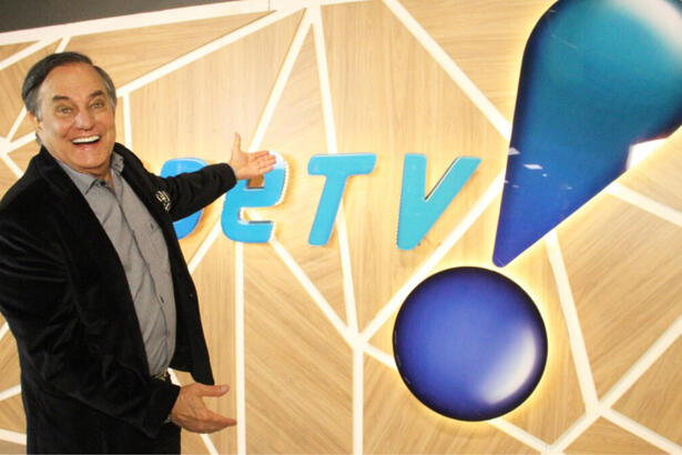 Ronnie Von apontando para o logo da RedeTV!, em uma parede na sede da emissora